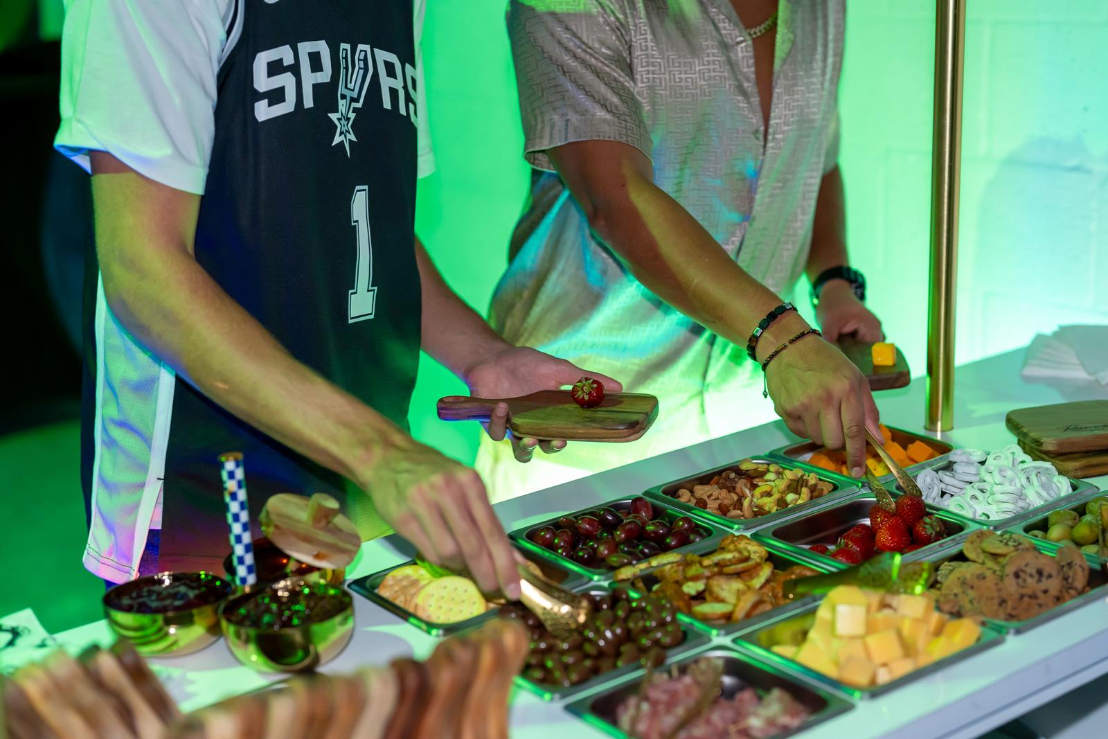The Runway Bites grazing bar under green LED glow, trays full of cheese, nuts and fruit
